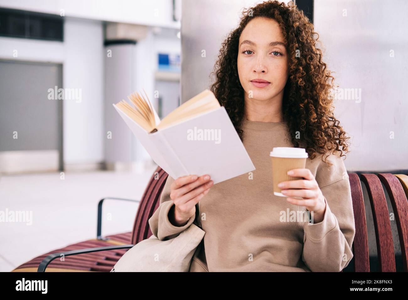 Junge Frau liest Buch mit Einweg-Tasse Kaffee Stockfoto