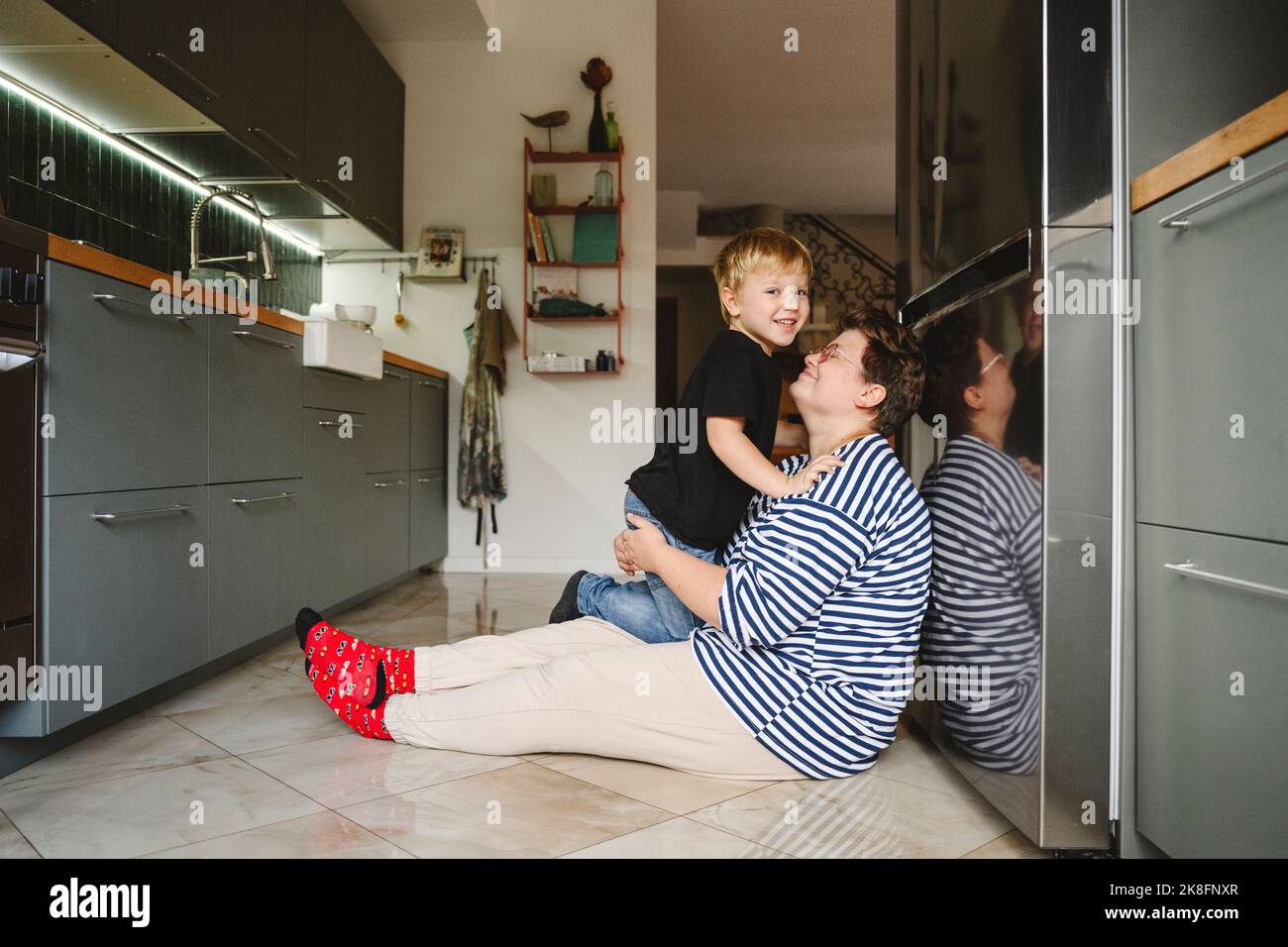 Glücklicher Sohn mit Mutter, die in der Küche auf dem Boden sitzt Stockfoto