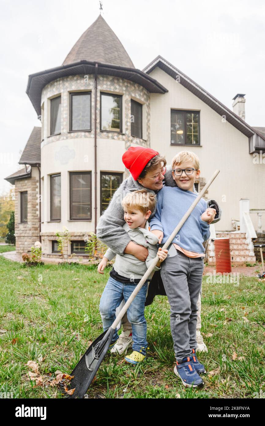 Glückliche Mutter umarmte Jungen, die vor dem Haus im Hinterhof standen Stockfoto