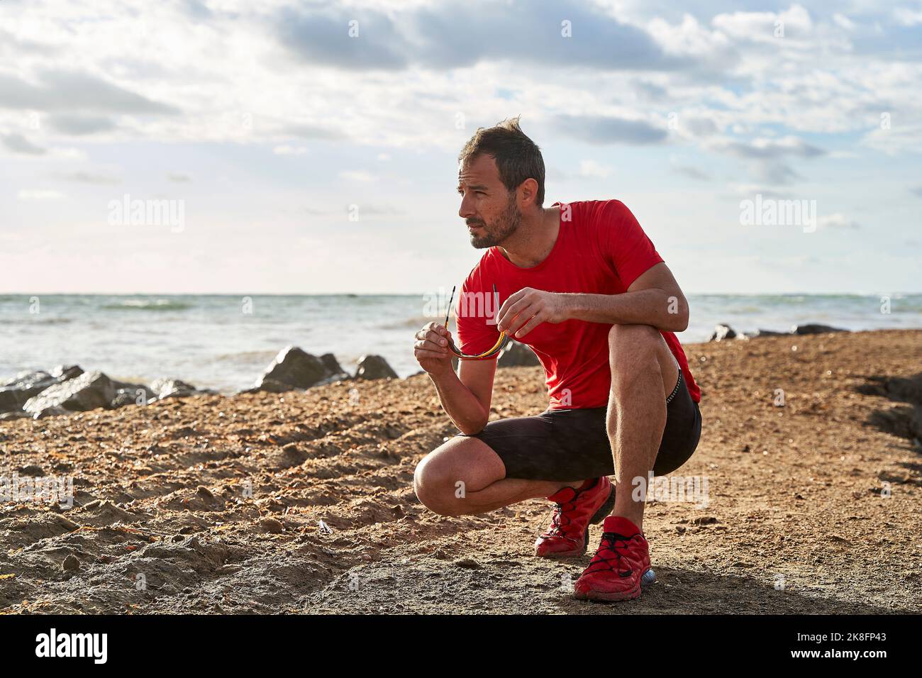 Mann mit Sonnenbrille, der am Strand hockt Stockfoto