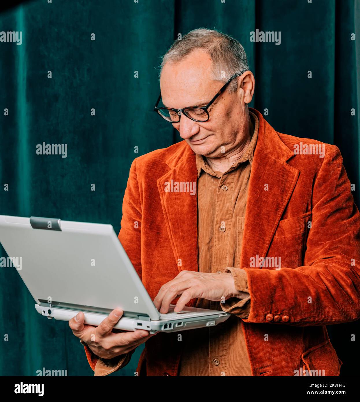 Älterer Mann, der vor dem Vorhang einen Laptop benutzt Stockfoto