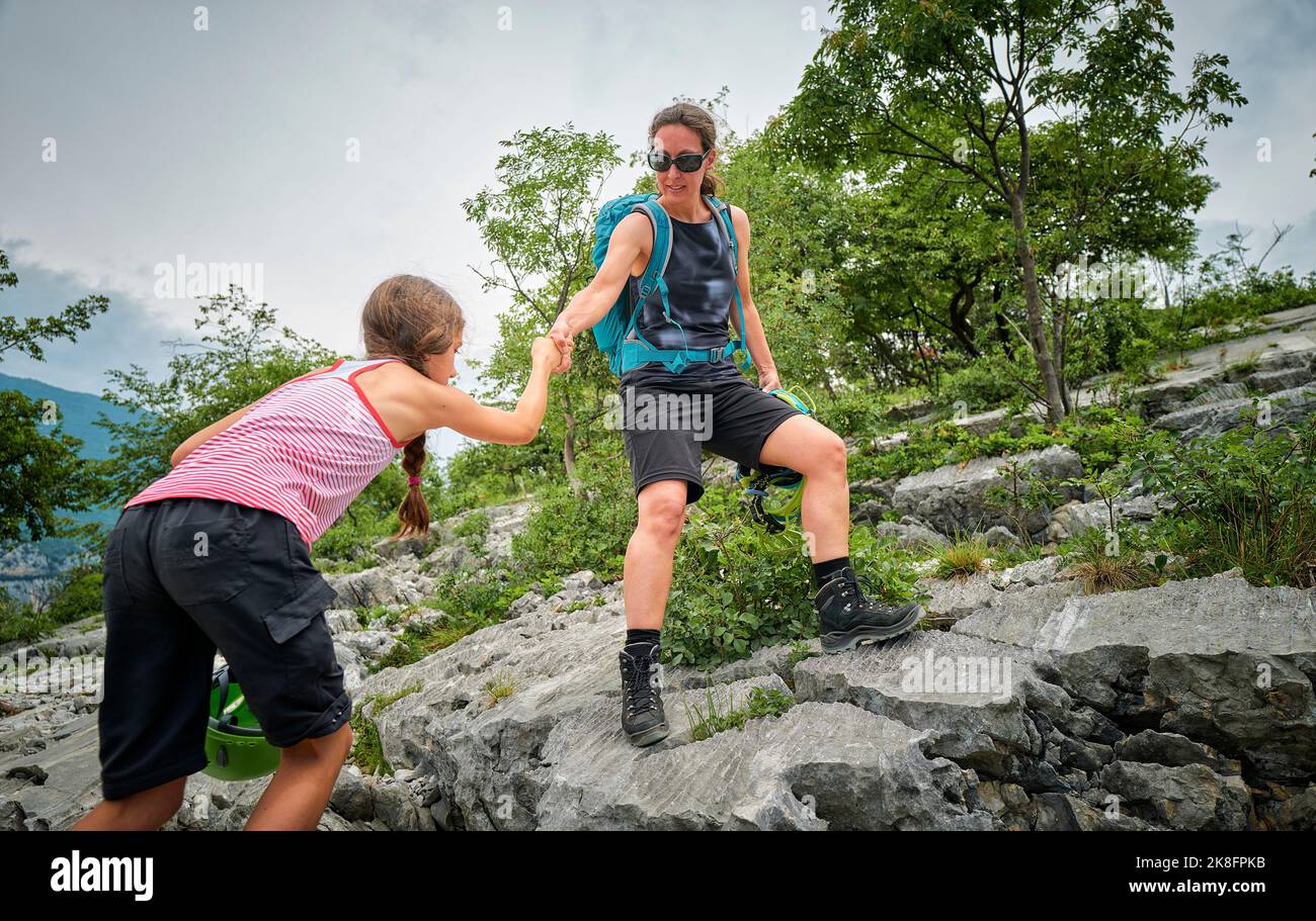 Frau, die die Hand der Tochter hält und dabei hilft, den Berg zu besteigen Stockfoto
