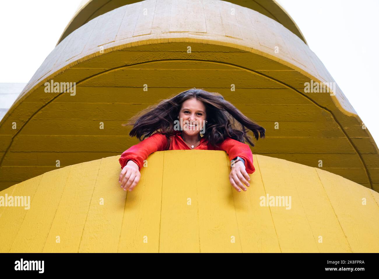 Glückliche junge Frau, die aus dem gelben Gebäude schaut Stockfoto