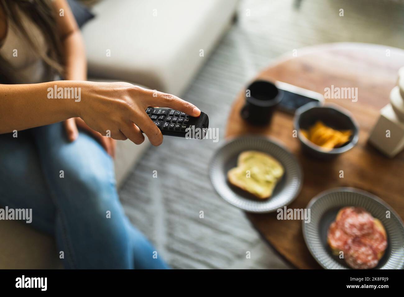 Junge Frau mit Fernbedienung sitzt zu Hause Stockfoto