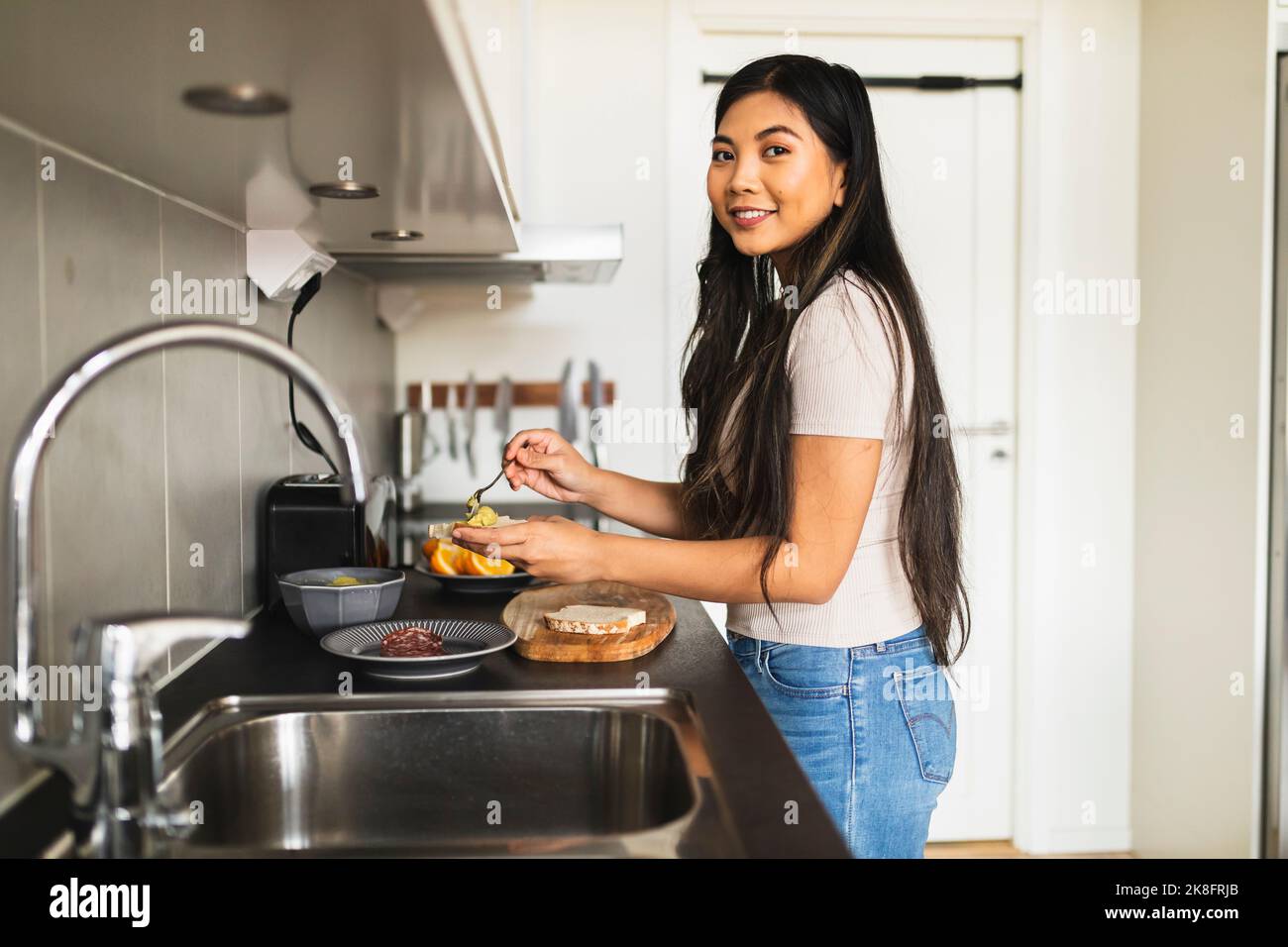 Lächelnde junge Frau, die zu Hause in der Küche Essen zubereitet Stockfoto