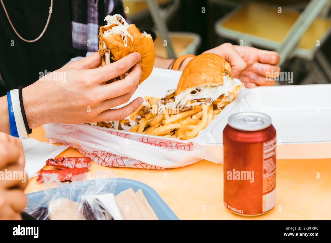 Hand eines Mannes, der Steak- und Käsesandwich am Tisch hält Stockfoto