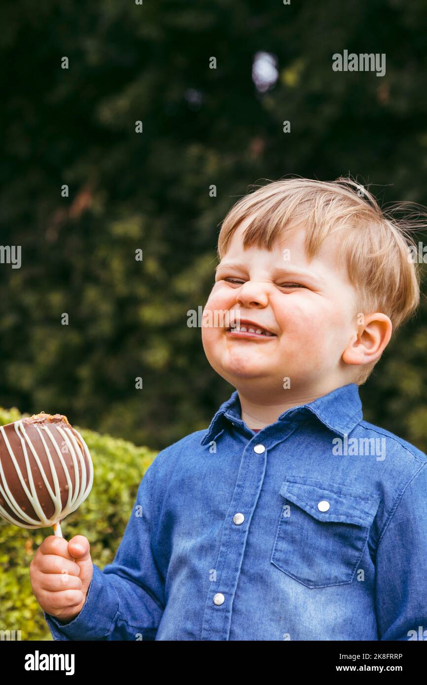 Junge macht Gesicht und hält taffigen Apfel im Park Stockfoto