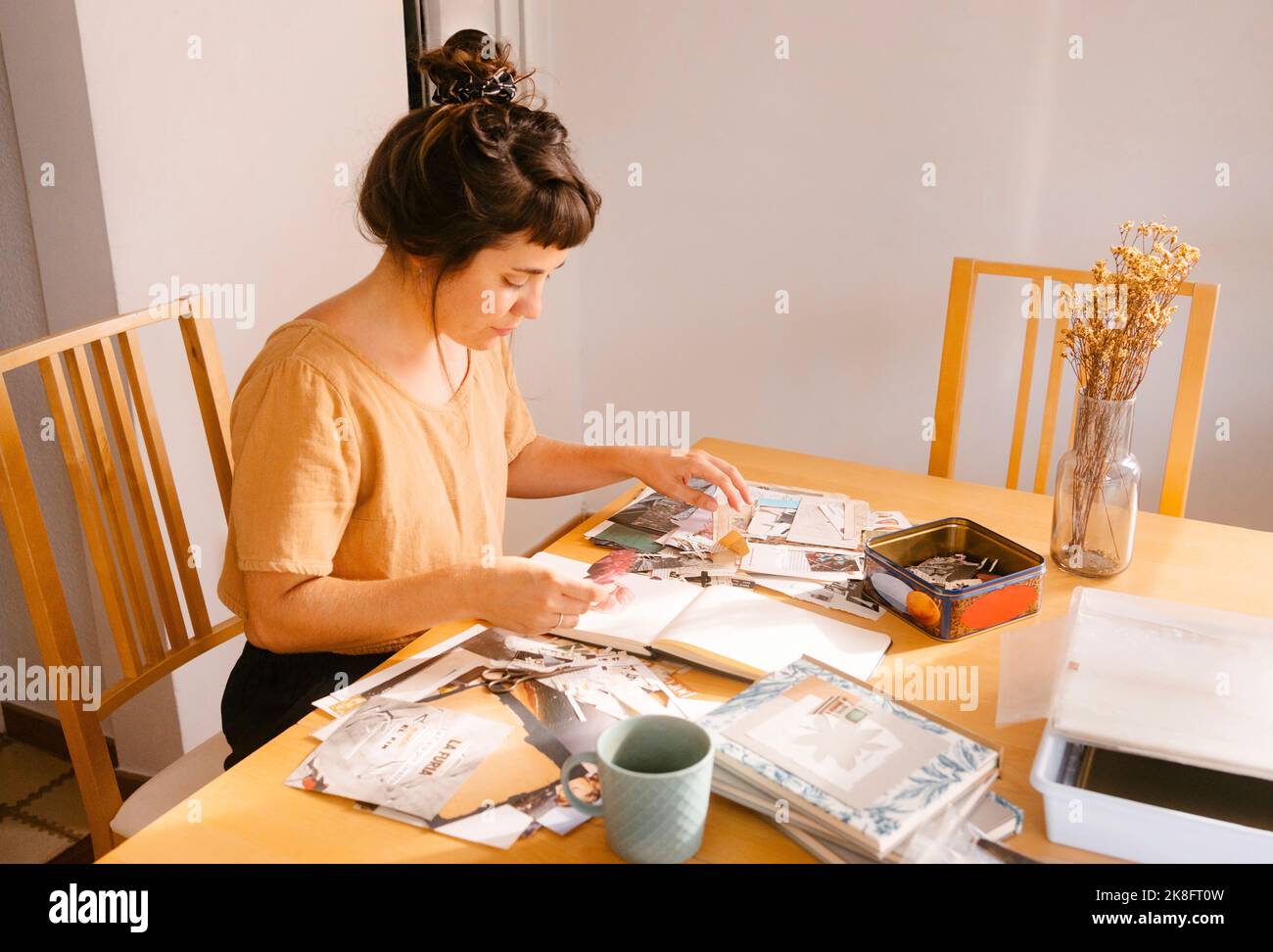 Freiberuflicher Mitarbeiter, der zu Hause am Schreibtisch Papierausschnitte im Buch arrangiert Stockfoto