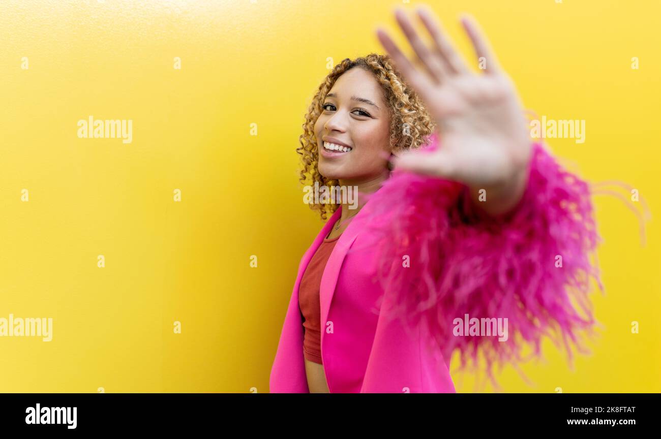 Lächelnde junge Frau gestikulieren stoppen in rosa Fell Blazer Stockfoto