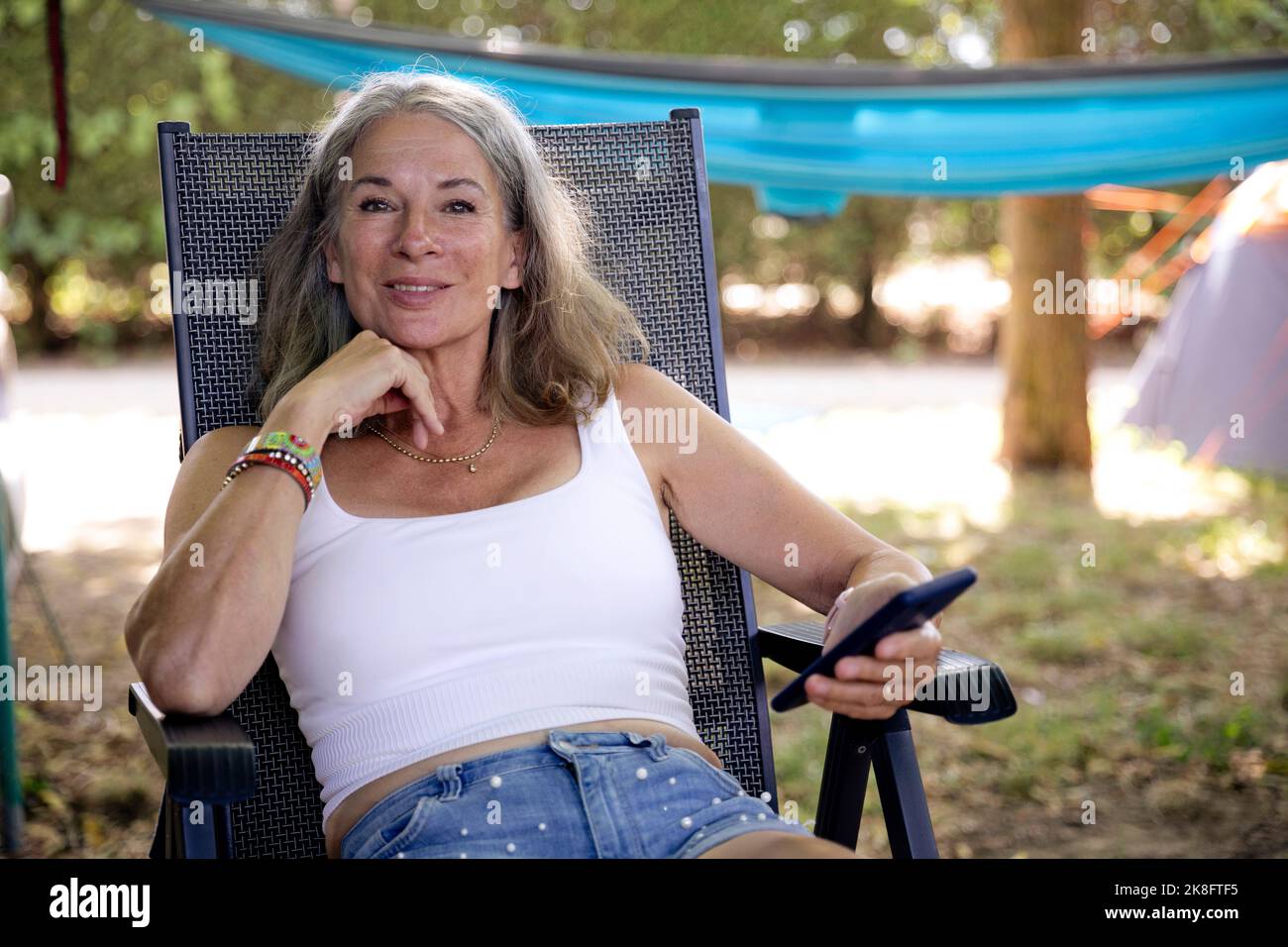 Lächelnde ältere Frau mit Smartphone auf Campingstuhl sitzend Stockfoto