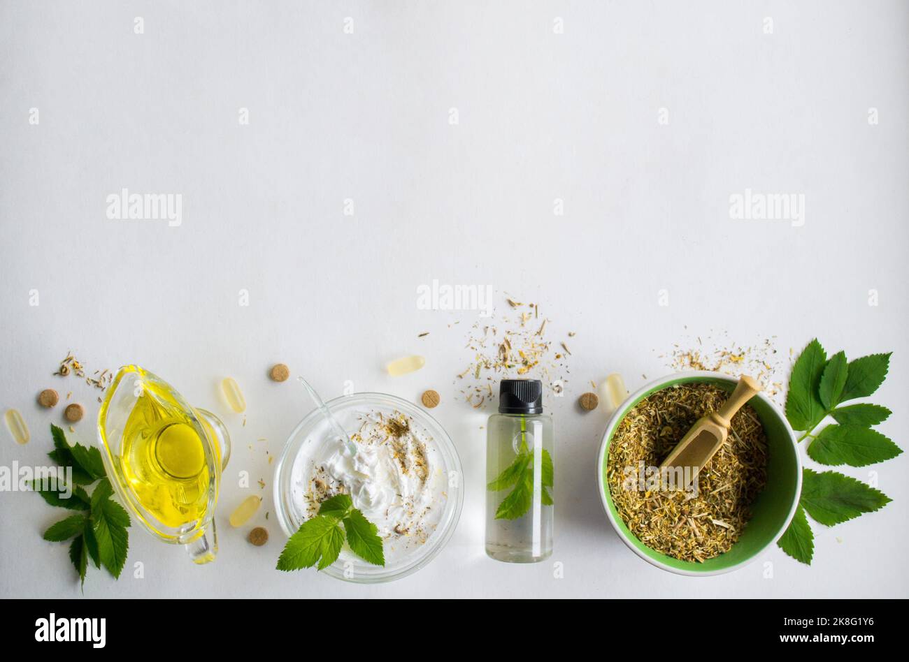 Alternative Medizin, Kräuterextrakt: Glas Öl, Schüssel mit weißer Essenz und Rühren. Schüssel mit gemahlenen trockenen Heilkräutern, grünen Blättern und Pillen. Stockfoto
