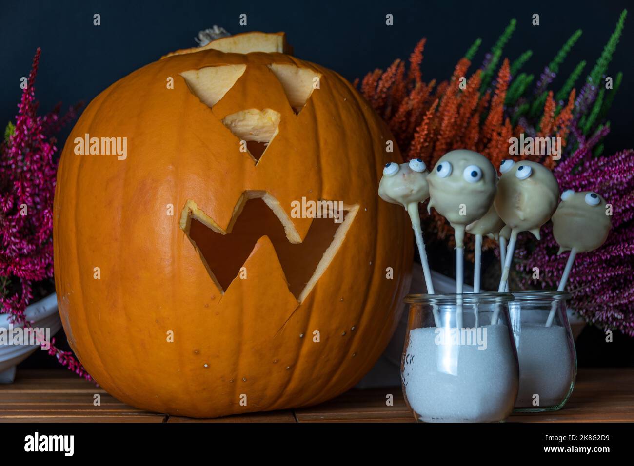 Die Geister kommen zu Kürbis der hinter herbstlichem Heidekraut in kräftig gestärkten Farben blühen.der Hintergrund in schwarz der Untergrund ein Tisch Stockfoto