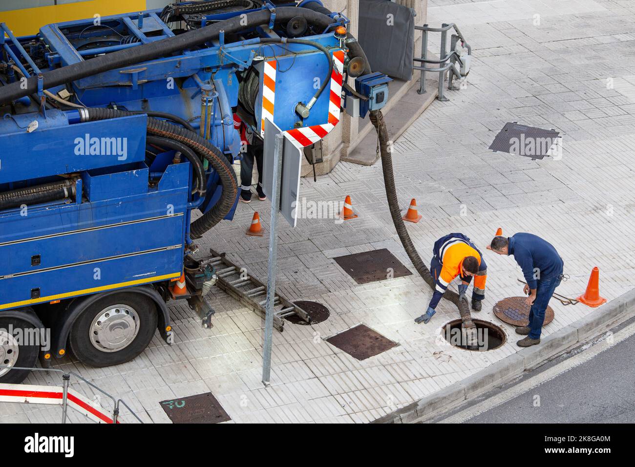 Galicien, Spanien; 30. september 2022: Kanalisationswagen und zwei Arbeiter auf der Straße, die die Blockierung eines Kanals mit einem Schlauch aufheben Stockfoto