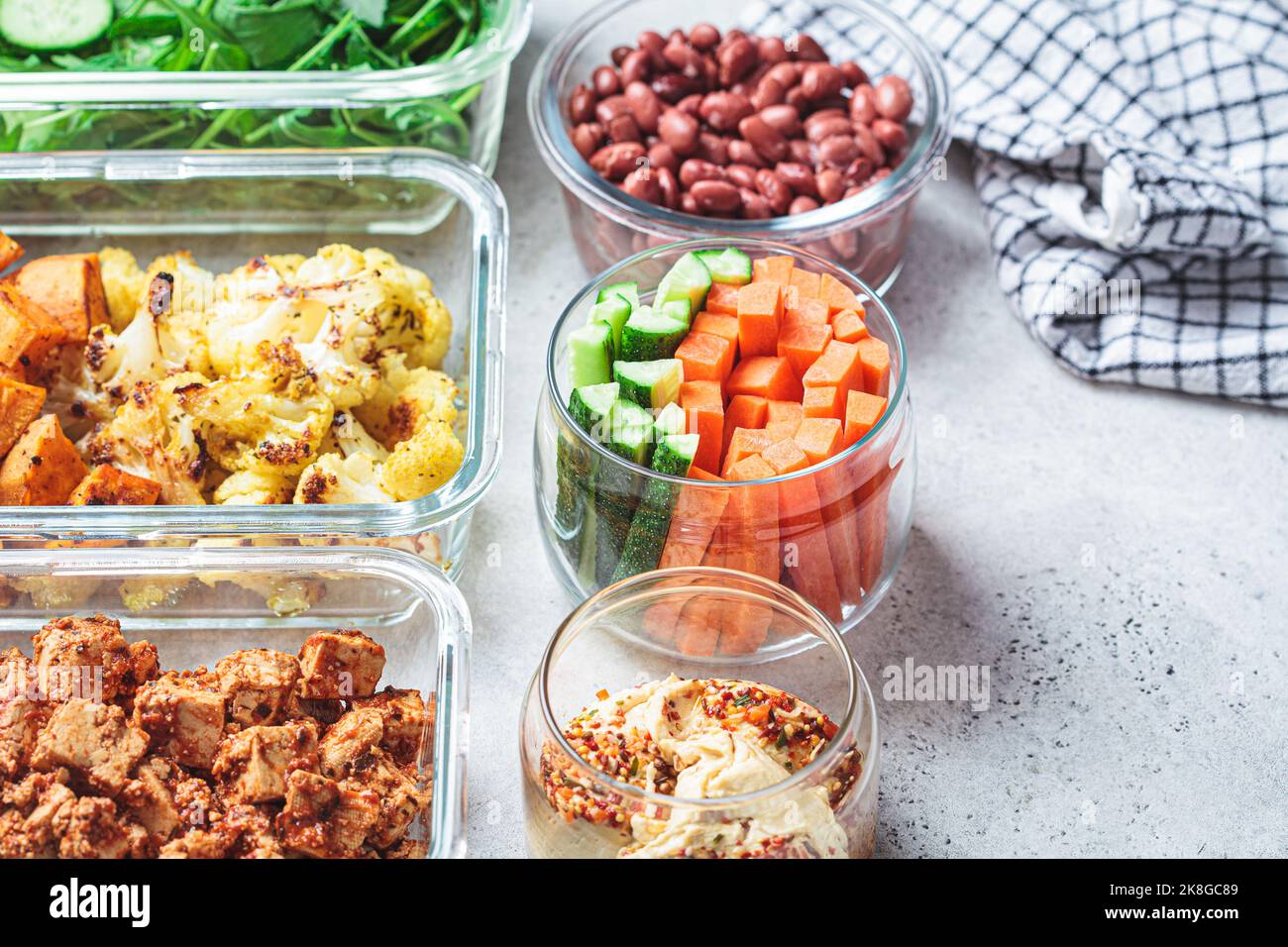 Vegane Behälter für die Zubereitung von Mahlzeiten mit gekochten Zutaten: Marinierter Tofu, Bohnen, gebackenes Gemüse, grüner Salat und Gemüsestöcke. Stockfoto