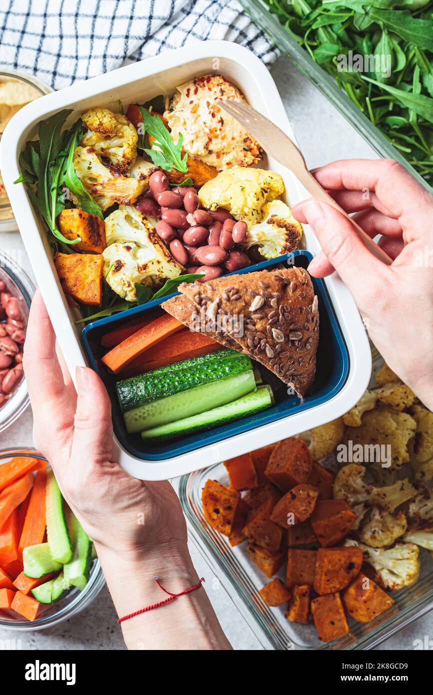 Kochen vegane Lunchbox flach legen. Hummus, Bohnen, gebackenes Gemüse, grüner Salat, Roggenbrot und Gemüsestöcke in einem Plastikbehälter, Draufsicht. Stockfoto