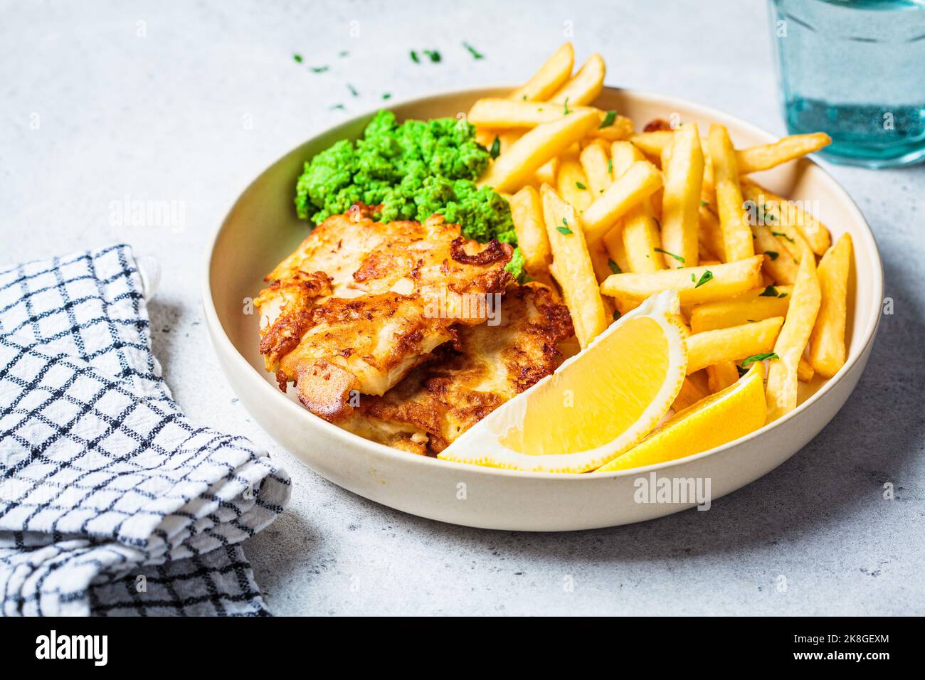 Fisch und Pommes. Kabeljau-Fisch im Teig mit pommes frites und pürierten grünen Erbsen auf weißem Teller, grauer Hintergrund. Englisches Essenskonzept. Stockfoto