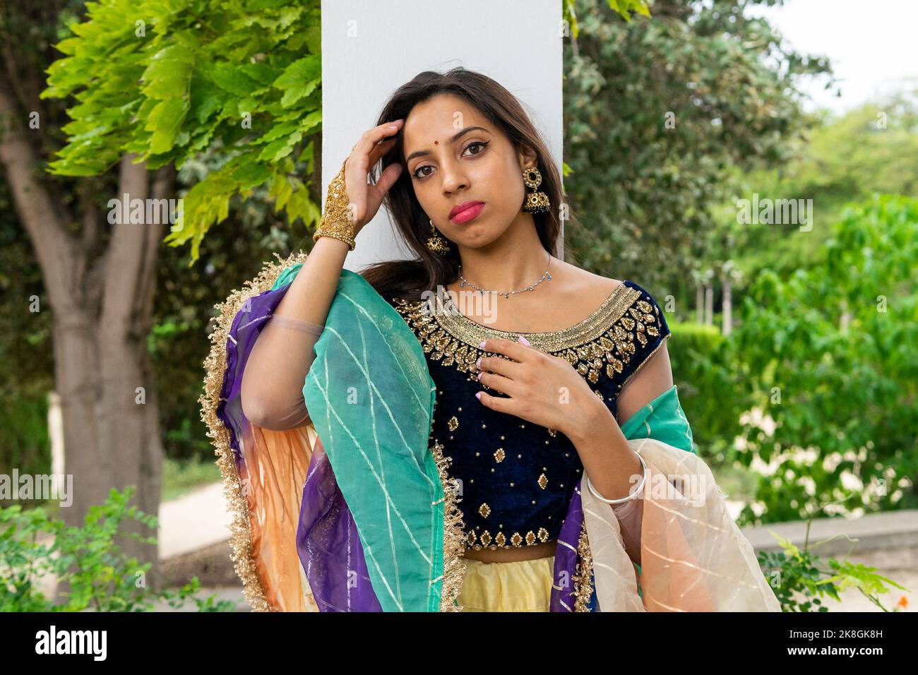 Junge ethnische indische Frau in stilvollem, traditionellem Sari und Schmuck, die im grünen Park wegschauen Stockfoto