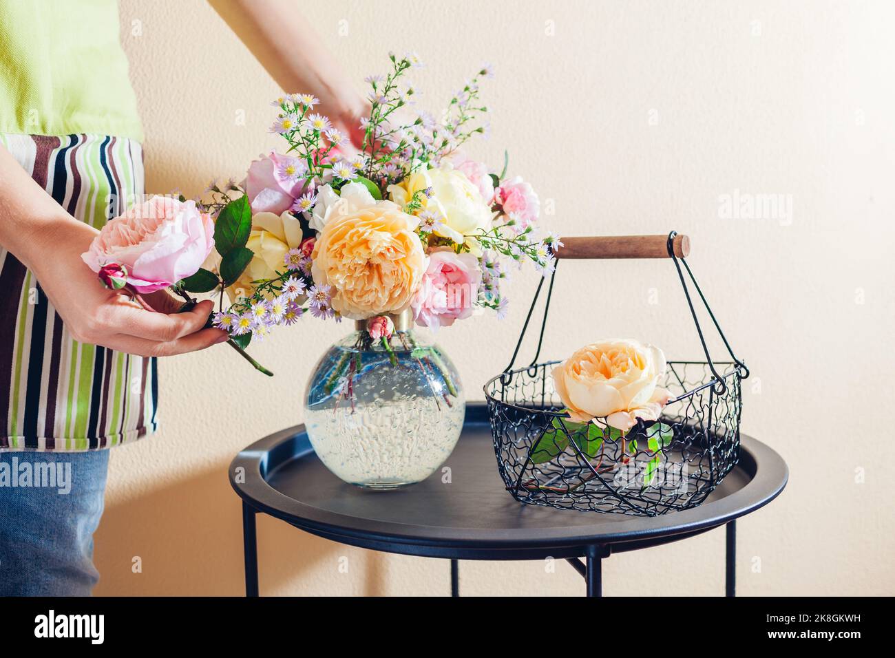 Nahaufnahme von frischen englischen Rosen. Frau macht Strauß in transparenter Vase mit orange gelb rosa Blumen auf dem Tisch zu Hause. Inneneinrichtung Stockfoto