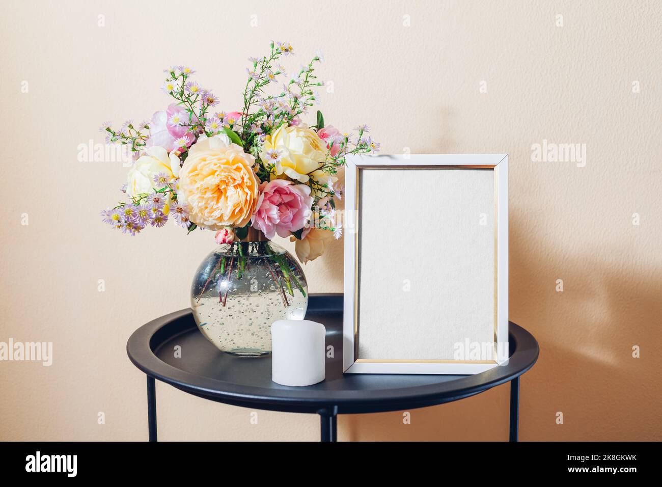 Leeres, leeres, leeres Modell eines weißen Fotorahmens mit Rosenstrauß und Kerze. Inneneinrichtung auf dem Tisch. Leerzeichen auf weißem Hintergrund Stockfoto
