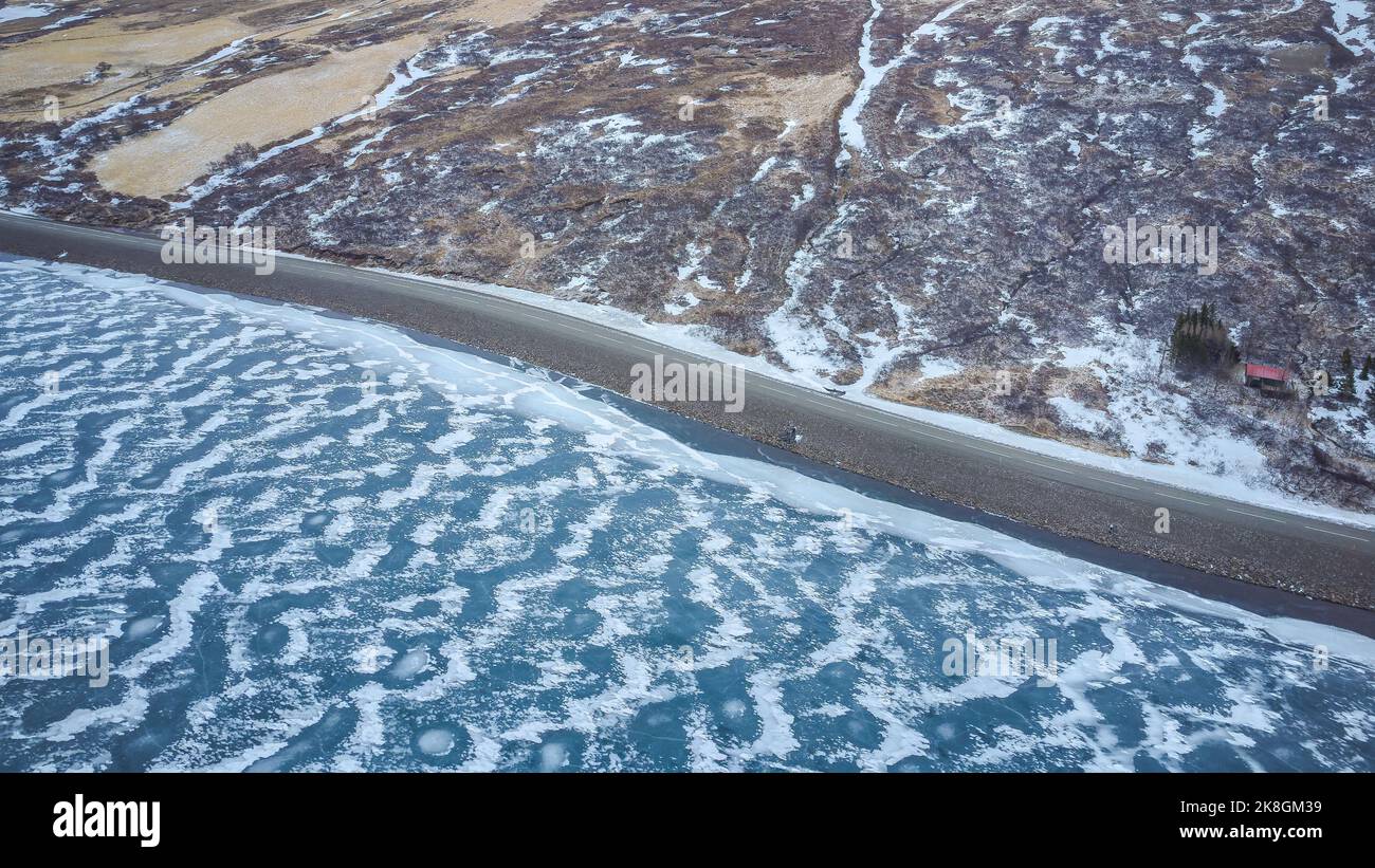 Luftaufnahme der unebenen Küste des ruhigen dunklen Meeres mit weißem Schnee bedeckt an kalten Wintertagen in Island Stockfoto