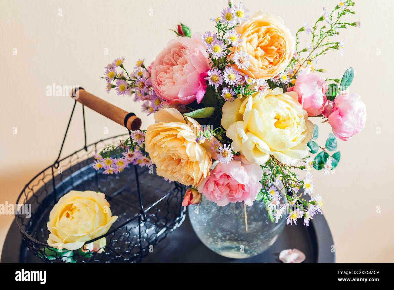 Frisches Bouquet von Rosenblüten in Glasvase auf den Tisch gelegt. Nahaufnahme von rosa gelben Blüten mit Korb. Einrichtung im Sommer Stockfoto