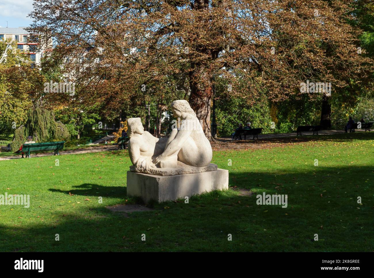 Pariser, die sich im Parc Montsouris mit einer Statue im Vordergrund ausruhen - Paris, Frankreich Stockfoto