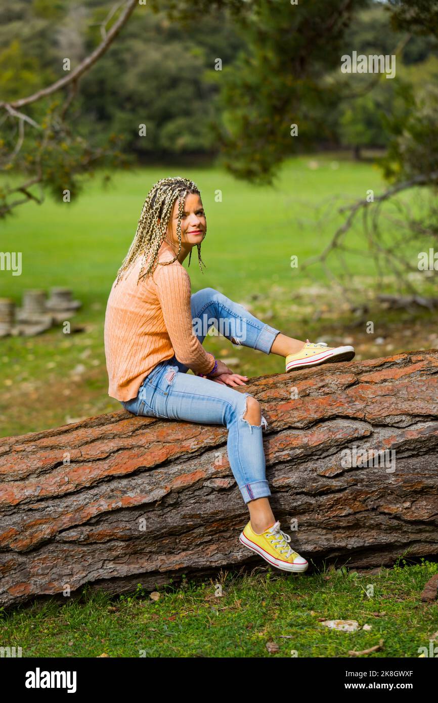 Attraktive reife Frau mit Fairhaarhaar blonde Haare Frisur und Freizeitkleidung Ganzkörper voller Länge Ganzkörper sitzen auf gefallenen Baum tunk Stockfoto