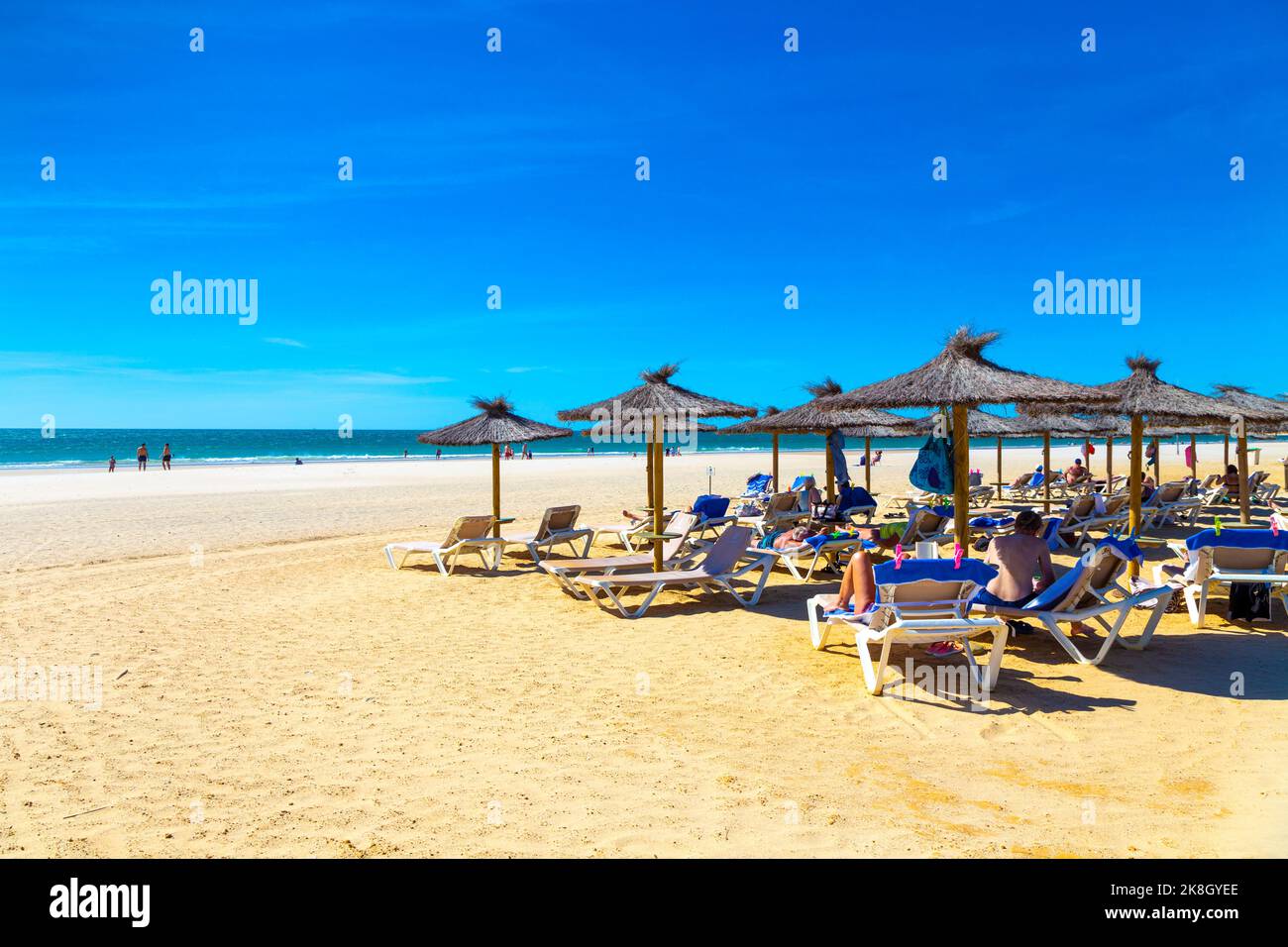 Strohsonnenschirme und Menschen auf Liegestühlen am Playa de la Barrosa, Cadaz, Spanien Stockfoto
