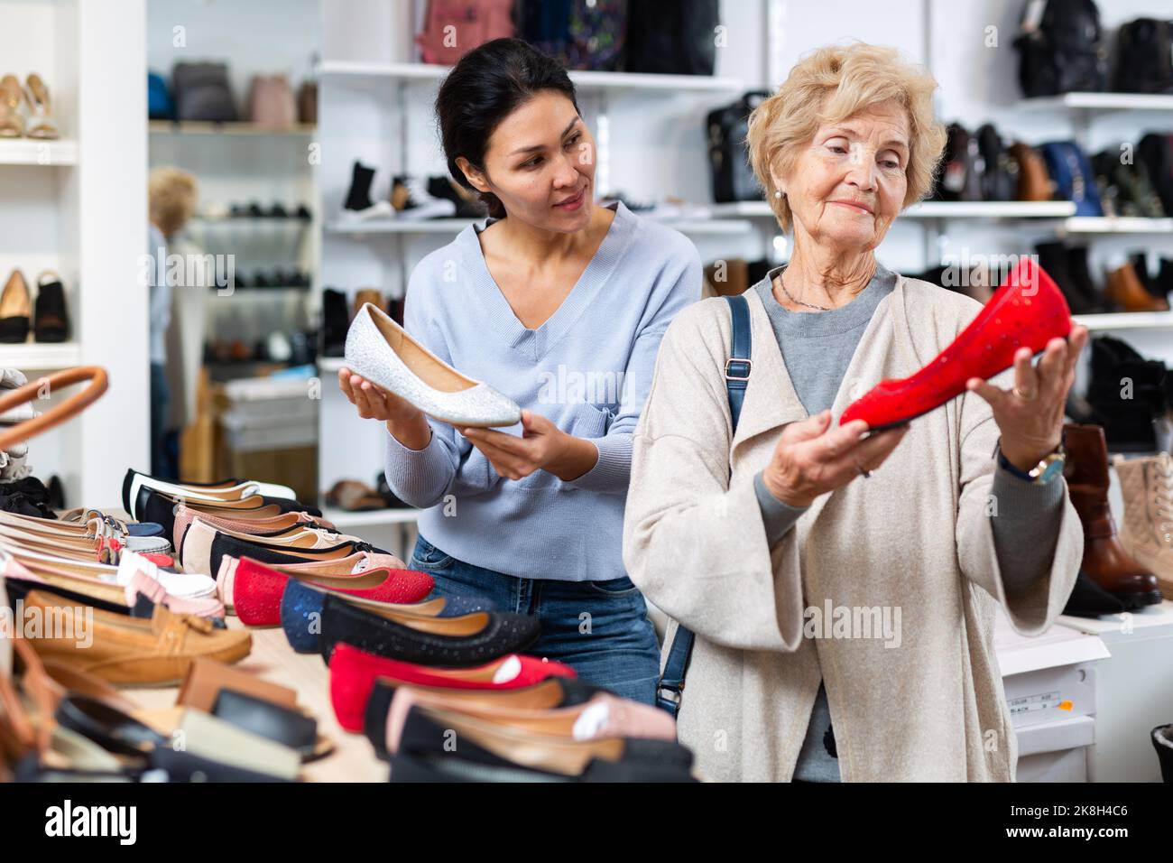 Verkäuferin hilft Oma bei der Auswahl neuer Schuhe Stockfoto