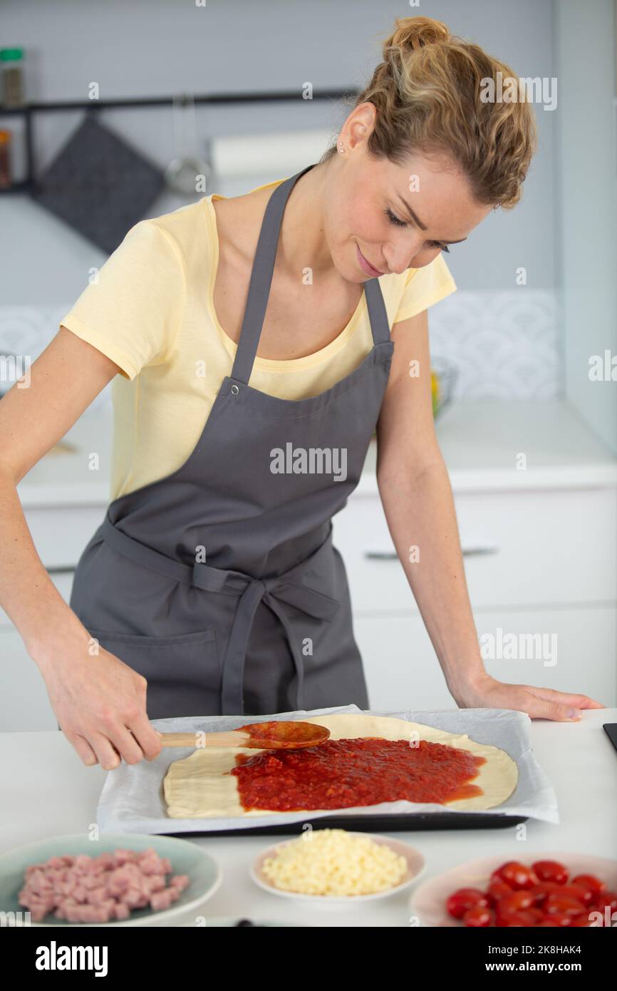 Nahaufnahme der Zugabe von Tomatensauce auf Pizzabasis Stockfoto