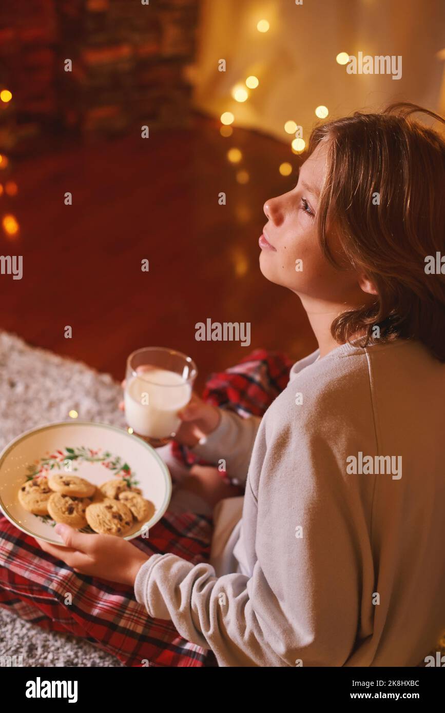 Netter Junge bereit für den Weihnachtsmann wartet mit Keksen und Milch. Der Glaube an das Märchen Stockfoto