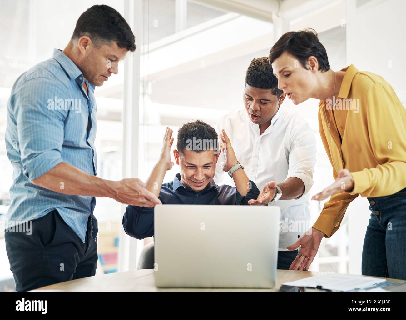Das alles geht mir über den Kopf. Ein junger Geschäftsmann, umgeben von anspruchsvollen Kollegen, während er an seinem Schreibtisch in einem Büro arbeitet. Stockfoto
