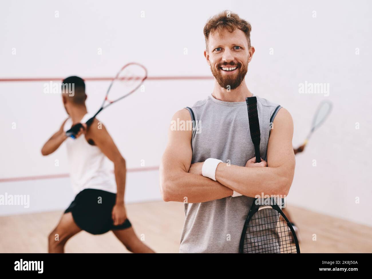 Es braucht Selbstvertrauen, um in diesem Spiel zu konkurrieren. Porträt eines jungen Mannes, der mit seinen Teamkollegen im Hintergrund ein Squashspiel spielt. Stockfoto