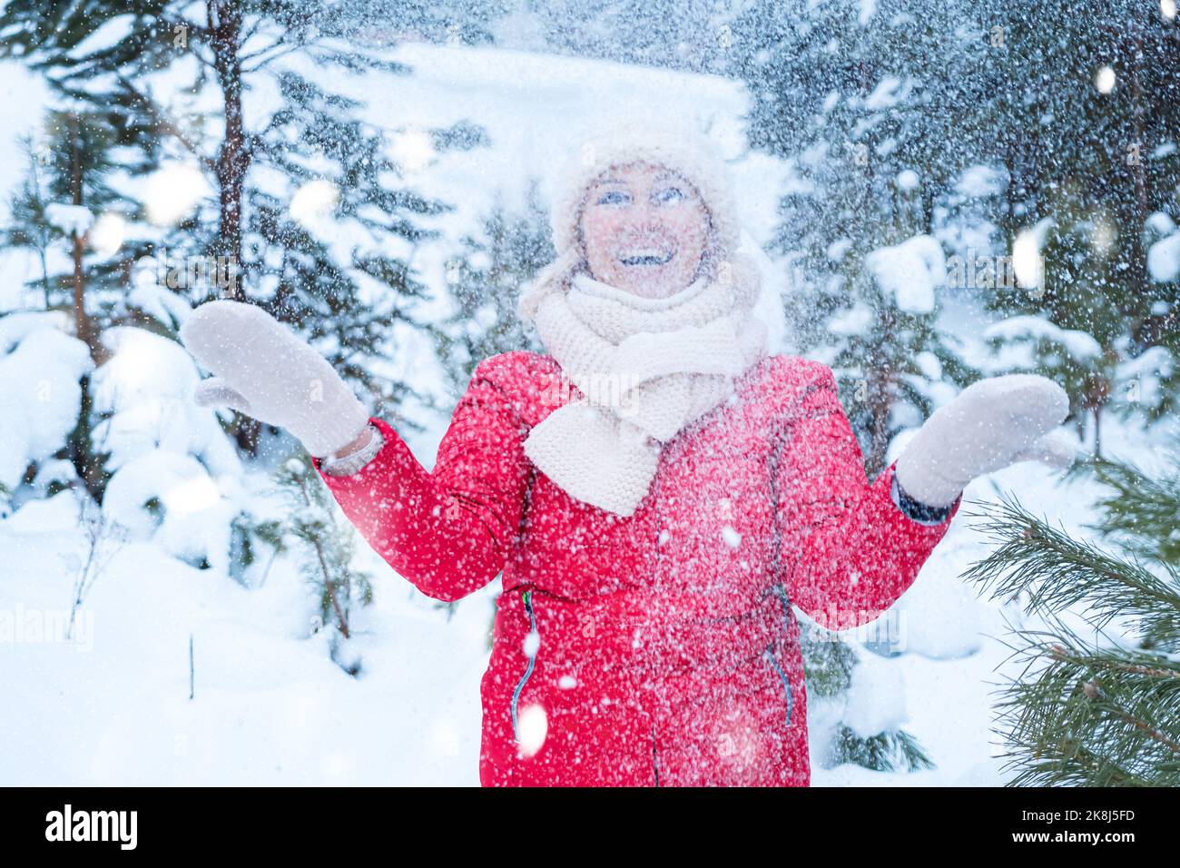 Frau mittleren Alters lächelt und spielt mit Schnee im Wald Stockfoto