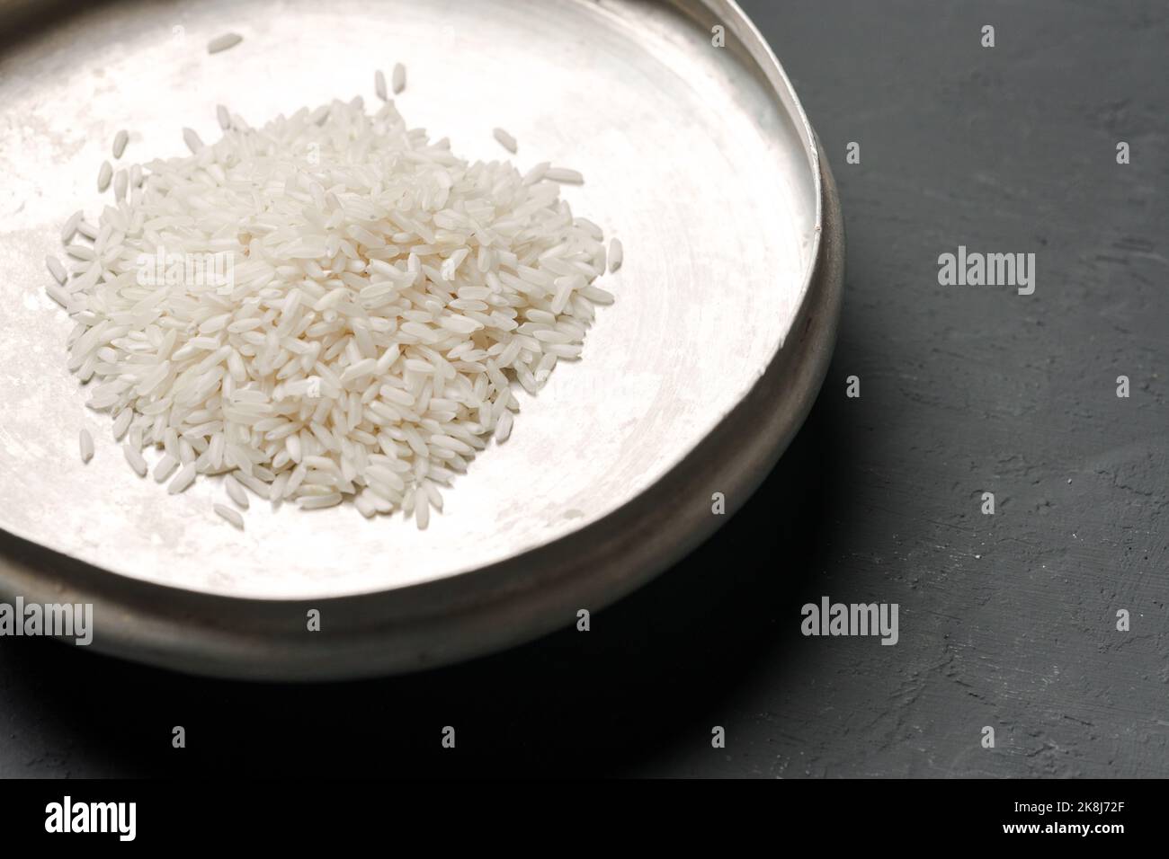 Haufen von trockenem Reis in einer Schüssel auf schwarzem Hintergrund, Mangel an Nahrung, Hunger-Konzept Stockfoto
