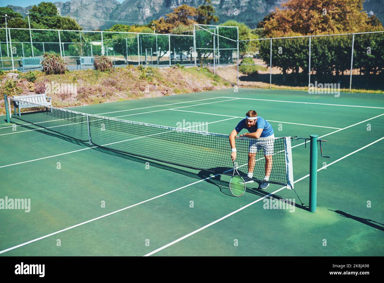 Die Champions gehen weiter, wenn alles andere scheitert. Ganzkörperaufnahme eines jungen männlichen Tennisspielers, der auf einem Tennisplatz im Freien über das Netz schlingende. Stockfoto