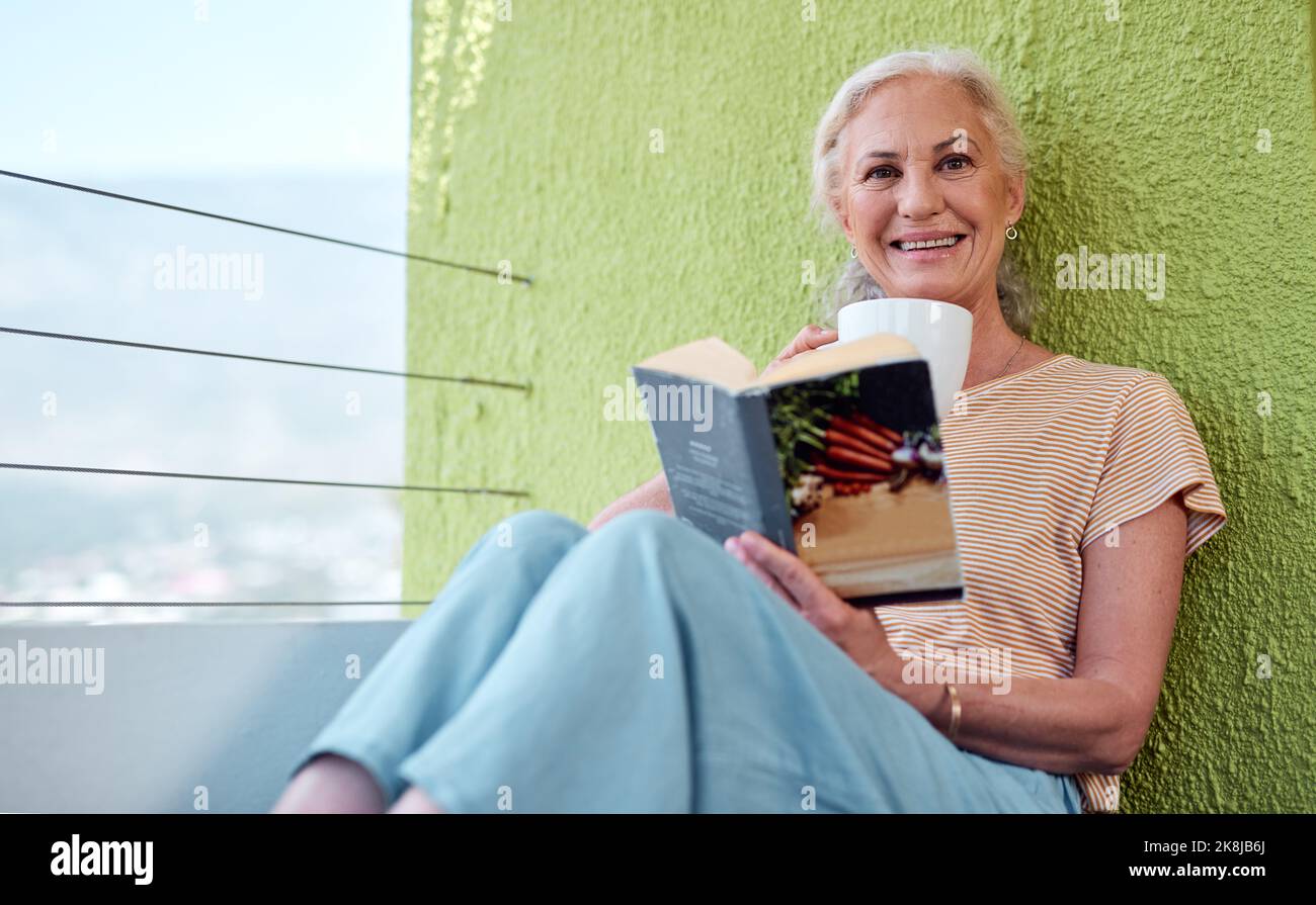 Die beste Art zu reisen, ohne zu Hause zu verlassen. Eine reife Frau liest ein Buch und hat Kaffee auf ihrem Balkon zu Hause. Stockfoto