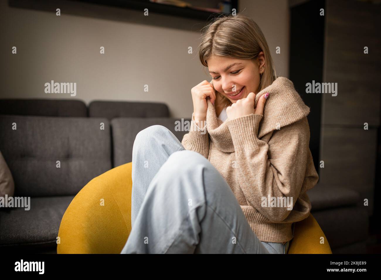 Glückliche junge Frau, die zu Hause auf dem Sofa sitzt. Portrait einer bequemen Frau in Winterkleidung, die sich auf dem Sessel entspannt. Portrait von schönen Mädchen lächeln ein Stockfoto