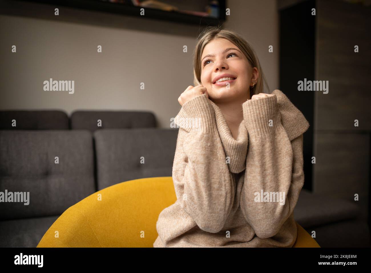 Glückliche junge Frau, die zu Hause auf dem Sofa sitzt. Portrait einer bequemen Frau in Winterkleidung, die sich auf dem Sessel entspannt. Portrait von schönen Mädchen lächeln ein Stockfoto