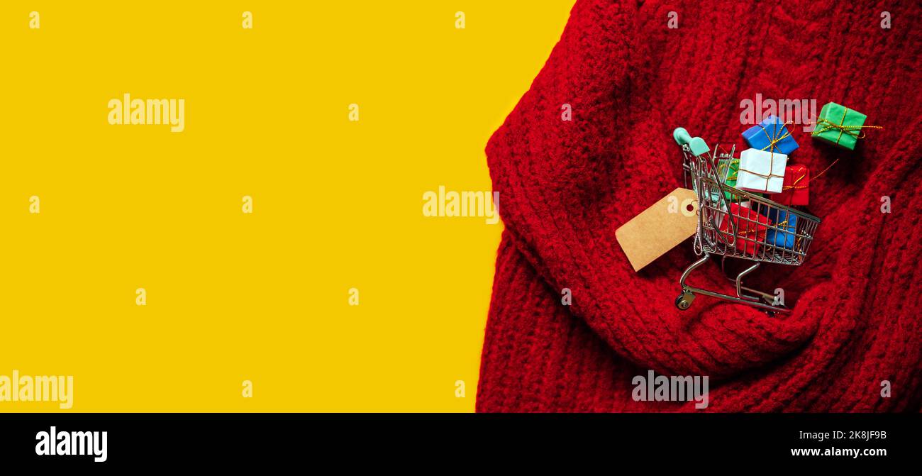 Weihnachtsbanner zum Einkaufen. Warenkorb mit vielen Geschenkboxen auf rotem Strick und gelbem Hintergrund Stockfoto