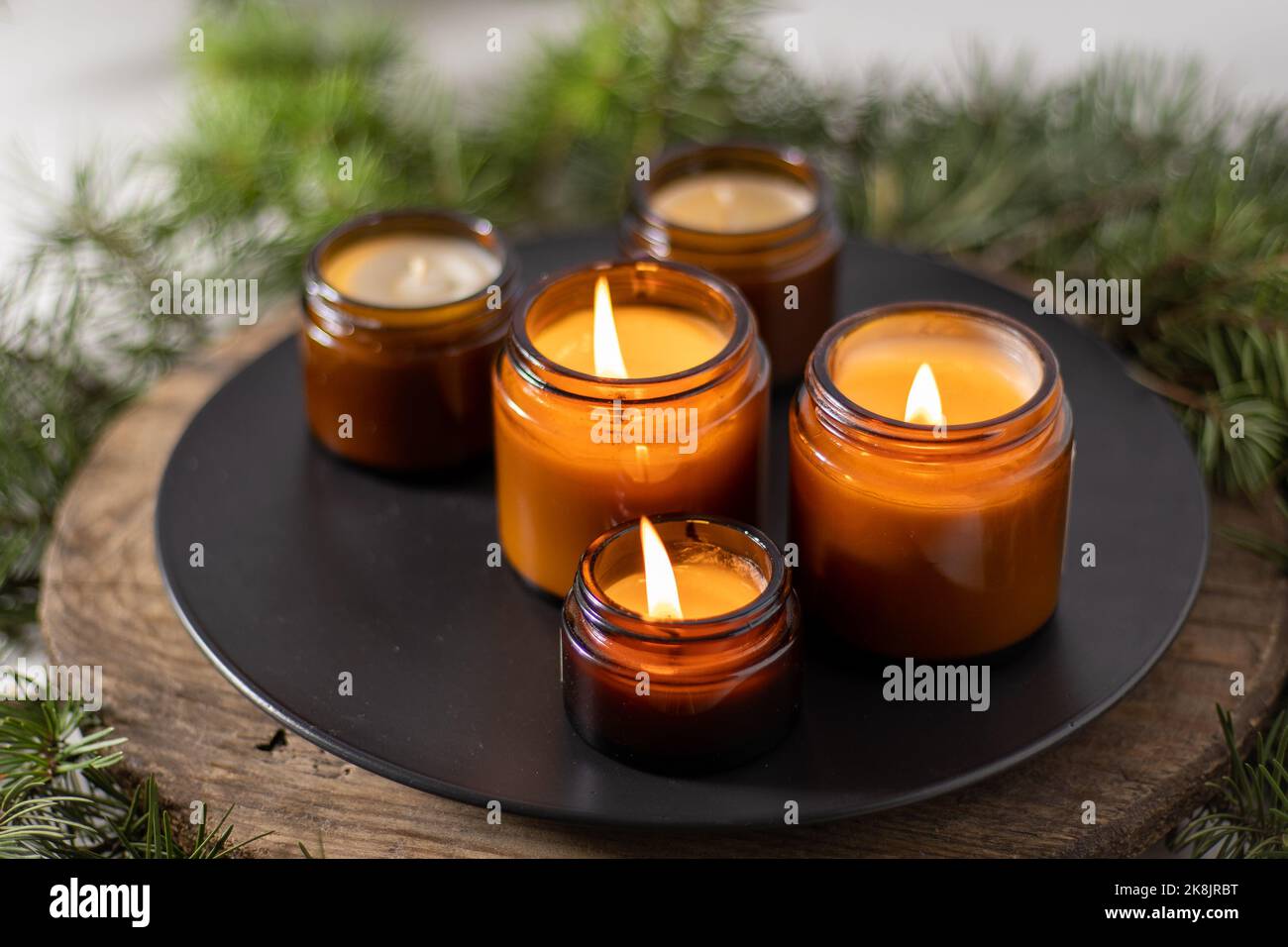 Sojalkerzen brennen in Gläsern. Komfort zu Hause. Kerze in einem braunen Glas. Duft und Licht. Handgemachte Duftkerze. Aromatherapie. Weihnachtsbaum und Winterstimmung. Gemütliche Einrichtung. Festliche Dekoration Stockfoto