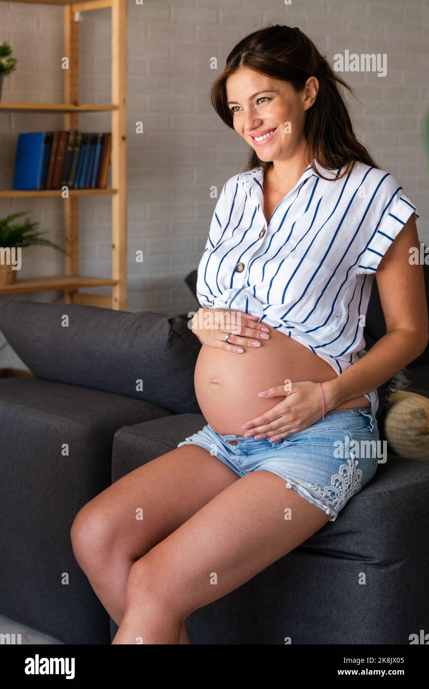 Schwangerschaft, Ruhe, Menschen und Erwartung Konzept. Glückliche, schwanger Frau, die zu Hause ihren Bauch berührt Stockfoto