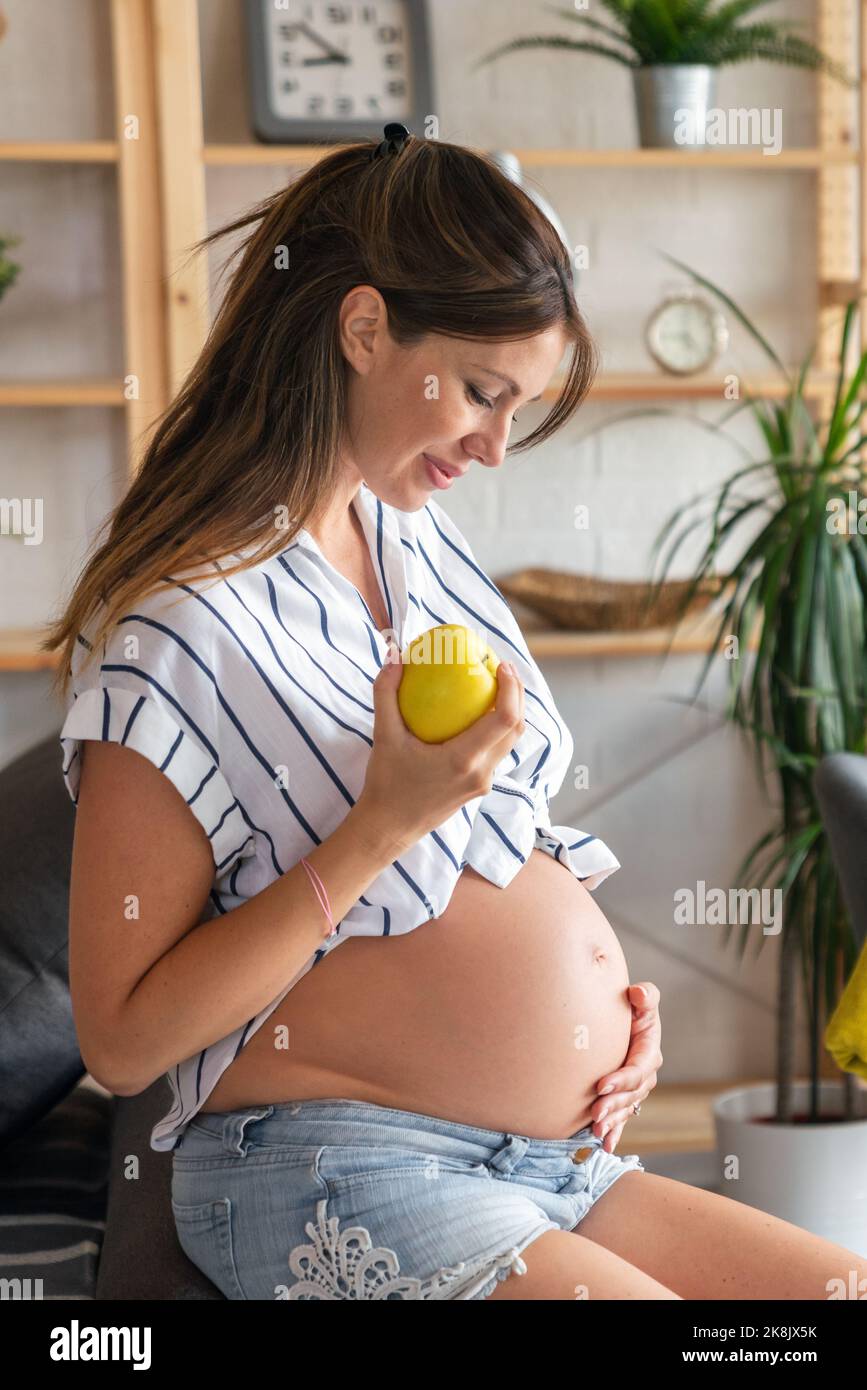 Schwangerschaft, Ruhe, Menschen und Erwartung Konzept. Glückliche, schwanger Frau, die zu Hause ihren Bauch berührt Stockfoto