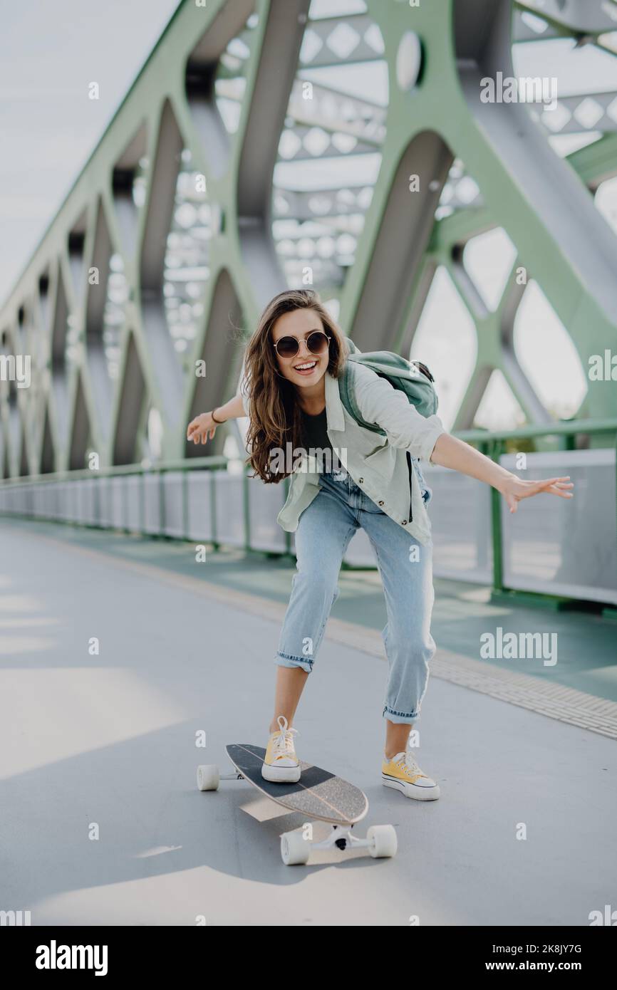 Junge Frau, die an der Stadtbrücke Skateboard fährt. Jugendkultur und Pendelkonzept. Stockfoto