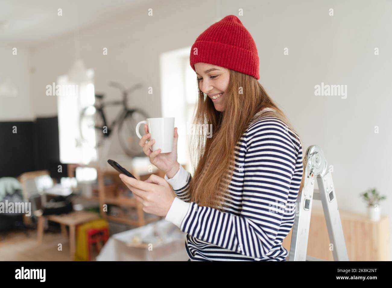 Glückliche junge Frau, die während der Renovierung ihrer Wohnung Pause hatte. Mit dem Telefon, auf der Suche nach Inspiration in sozialen Medien. Stockfoto