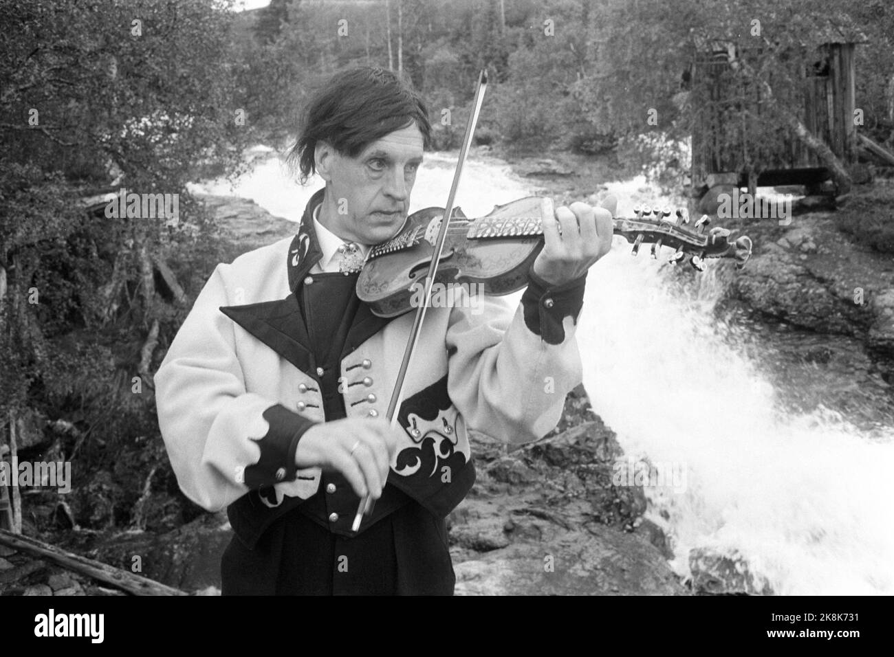 Osa spielt harding fiddle mit wasserfall im hintergrundfoto Fotos und
