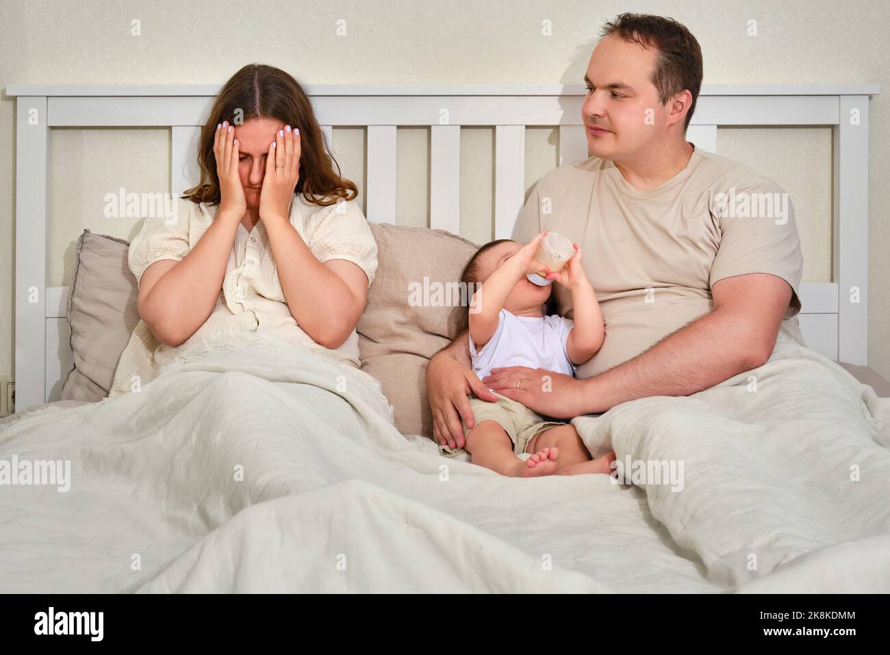 Ein Vater mit einem kleinen Jungen und einer Mutter, die bei postpartaler Depression weint, Eltern und ein Kleinkind auf einem Heimbett. Probleme eines Mannes und einer Frau mit einem Stockfoto