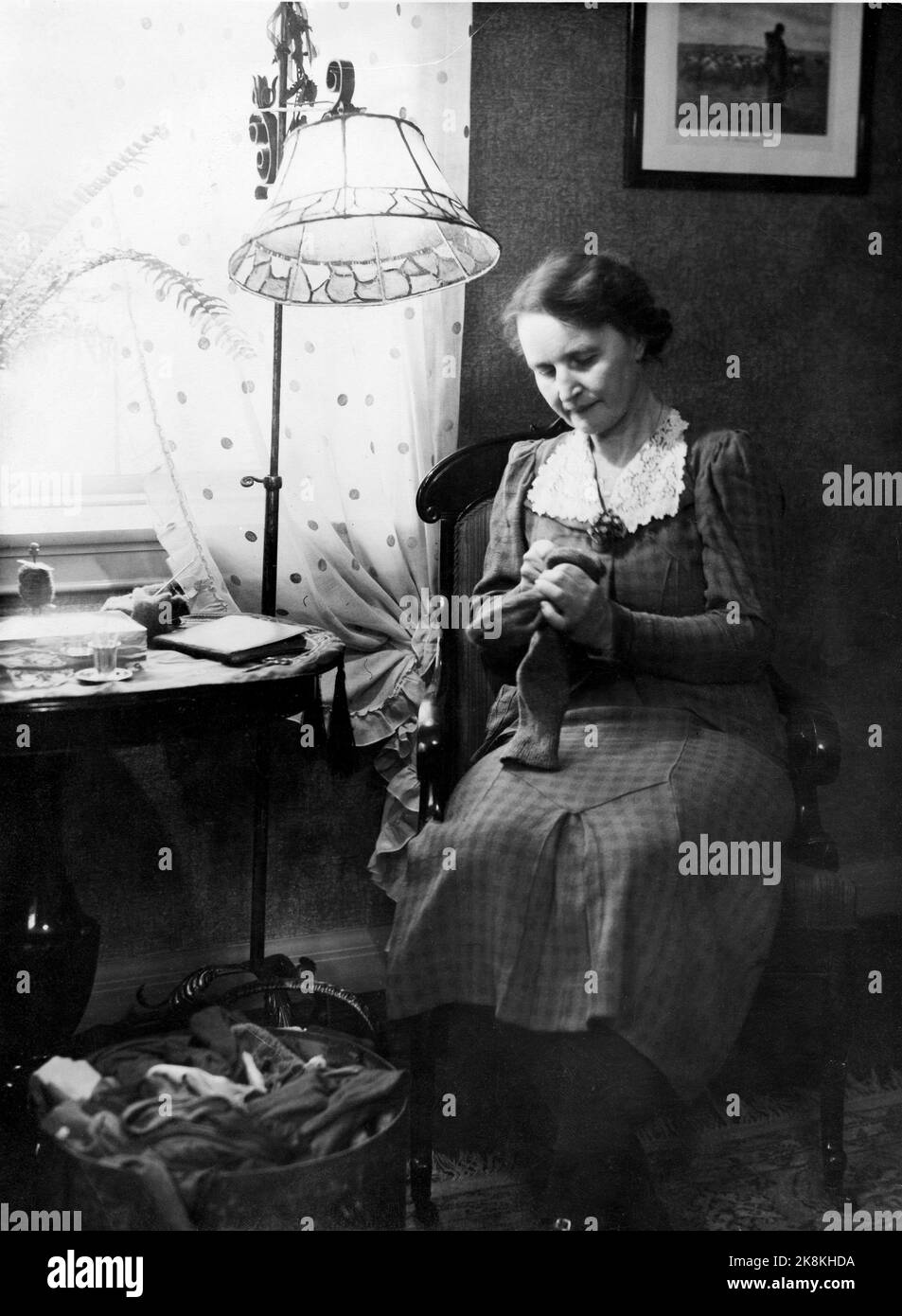 Oslo ca. 1930 - altmodisch. Ältere Frau sitzt und hält Strümpfe unter einer Stahllampe an. Hausarbeit / Nadelarbeit. Foto: NTB / NTB Stockfoto