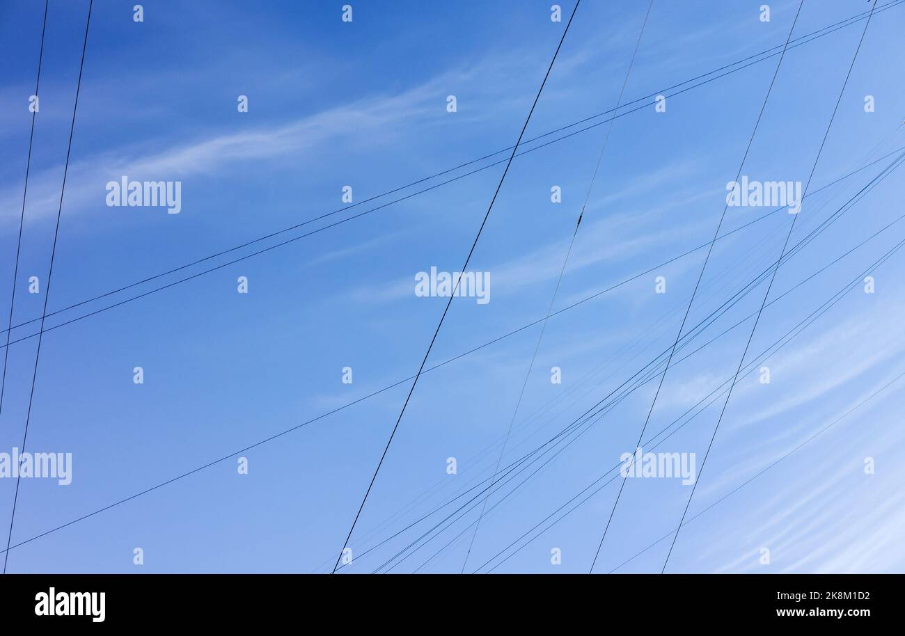 Stromkabel und Drähte sind unter blauem bewölktem Himmel, städtische Elektrizität abstraktes Hintergrundfoto Stockfoto