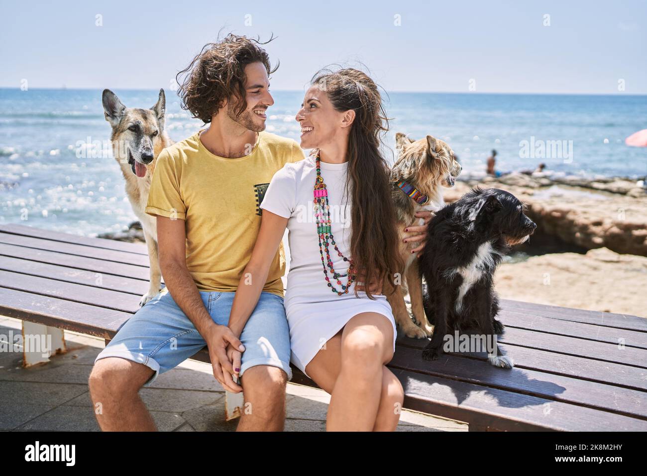 Mann und Frau Paar lächeln selbstbewusst und umarmen sich am Meer mit Hunden Stockfoto
